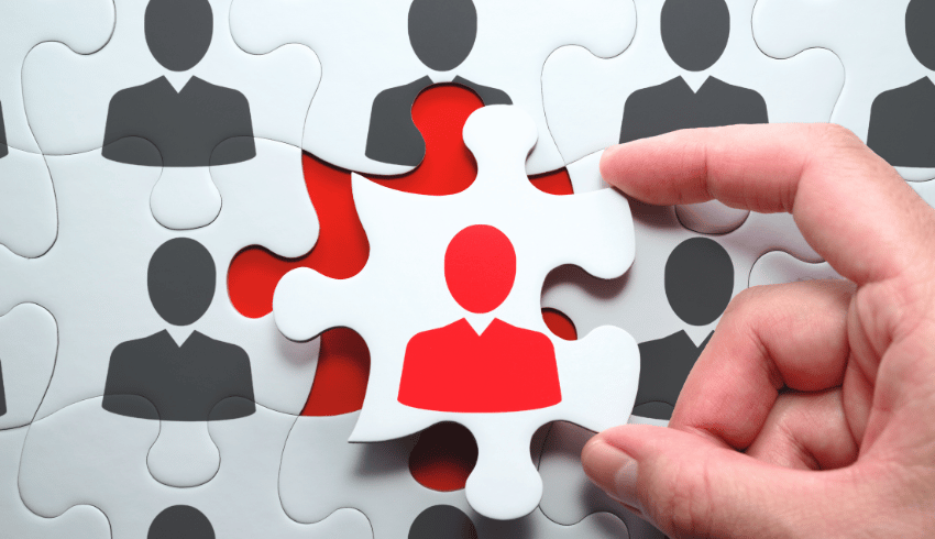 Hand selecting a puzzle piece with a red head and shoulders on it, representing teacher recruitment