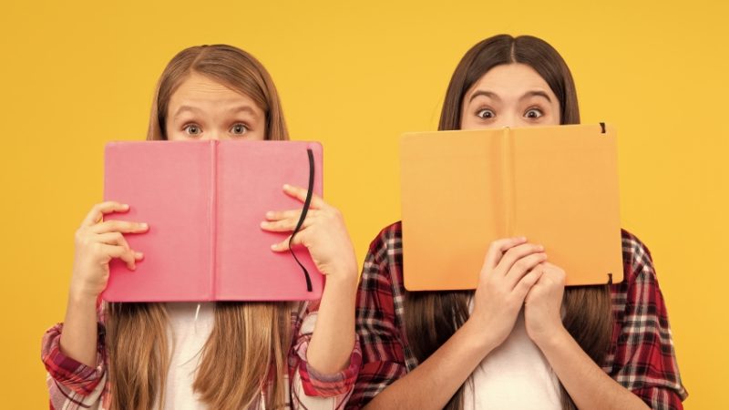 Two girls peeking over books, representing teaching English Literature