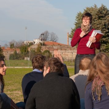 Photo of a teacher addressing a class sat outdoors in green space