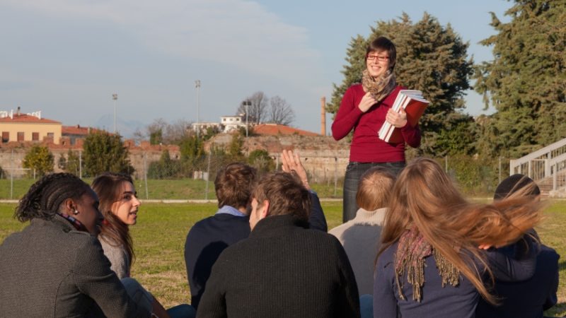 Photo of a teacher addressing a class sat outdoors in green space