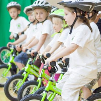 A group of schoolchildren learning to ride bikes indoors