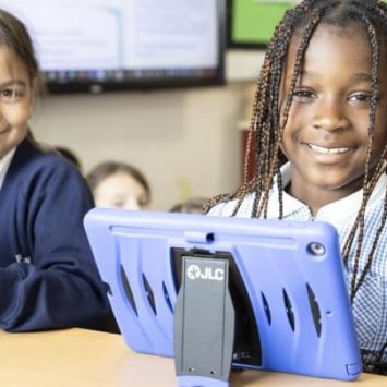 Two school girls with tablets sitting at a desk