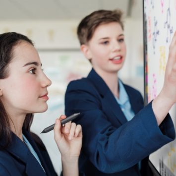 Two secondary school students standing next to an interactive whiteboard