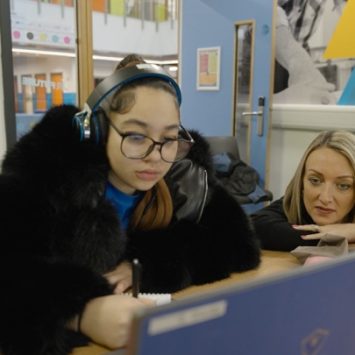 A student sitting at a desk with a laptop next to a teacher