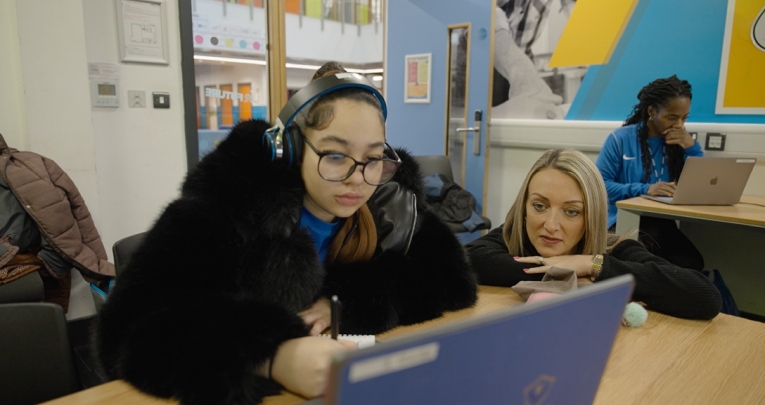 A student sitting at a desk with a laptop next to a teacher