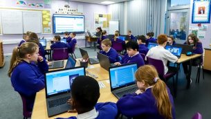 A group of secondary school children working with laptops in a classroom