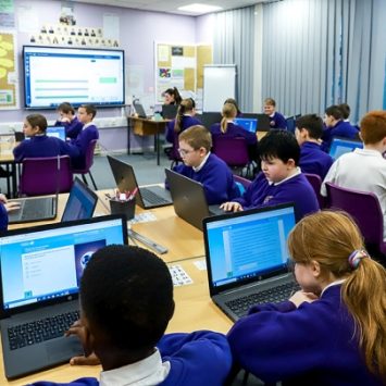 A group of secondary school children working with laptops in a classroom