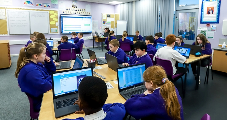 A group of secondary school children working with laptops in a classroom