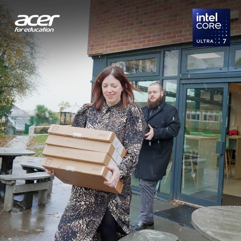 A teacher carrying four laptops in their packaging