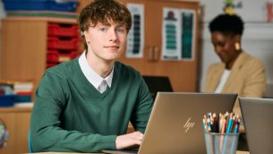 A secondary school student sitting at a desk with a laptop