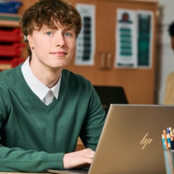 A secondary school student sitting at a desk with a laptop