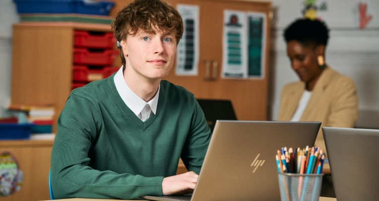 A secondary school student sitting at a desk with a laptop
