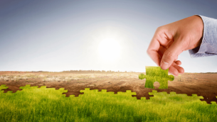 Hand placing green jigsaw piece on barren land, representing climate action plan