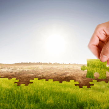 Hand placing green jigsaw piece on barren land, representing climate action plan
