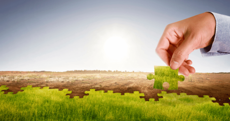 Hand placing green jigsaw piece on barren land, representing climate action plan