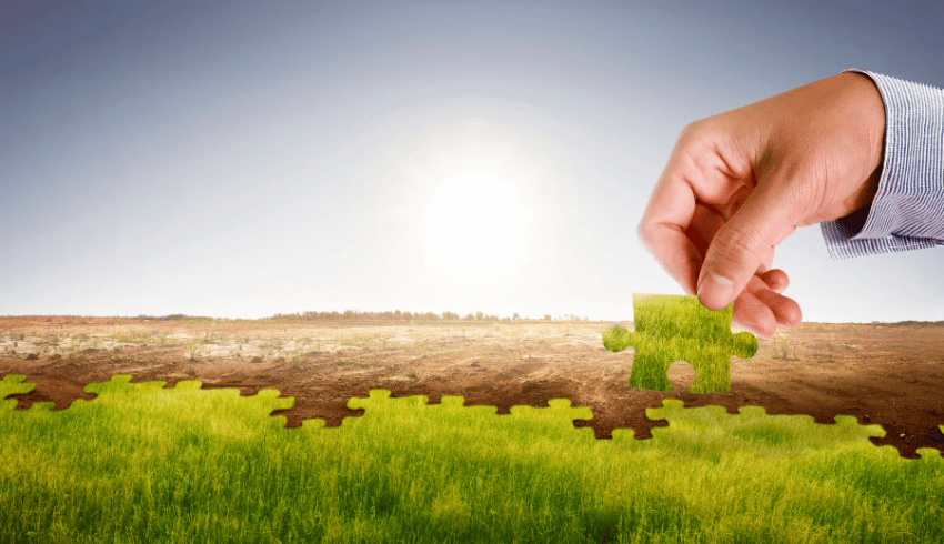 Hand placing green jigsaw piece on barren land, representing climate action plan