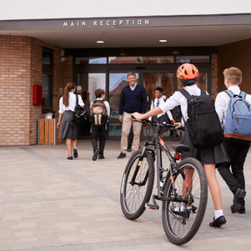 A group of secondary school children entering a school; one is wheeling a bike