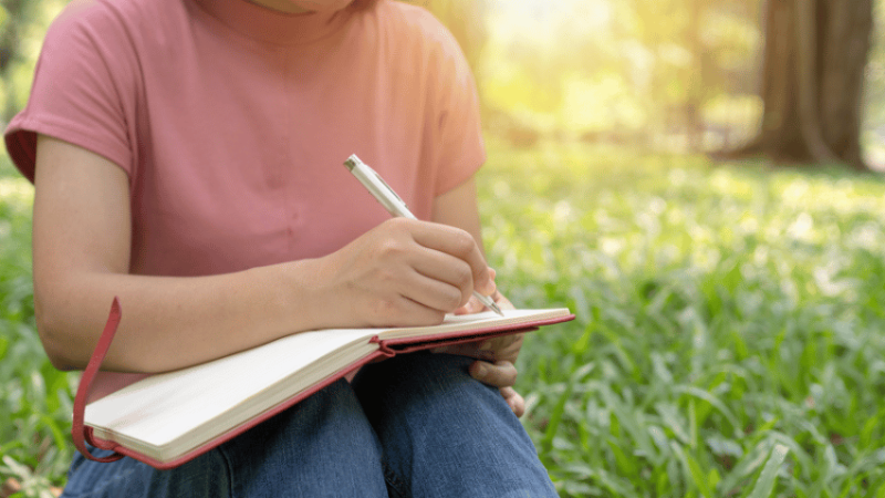 Person writing in notebook outdoors, representing nature poetry