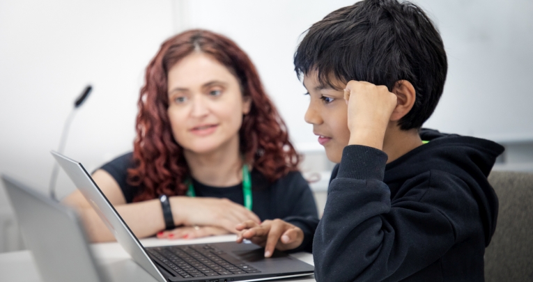 A teacher helping a schoolboy using a laptop
