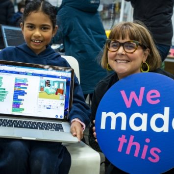 A school girl standing and holding a laptop next to a teacher