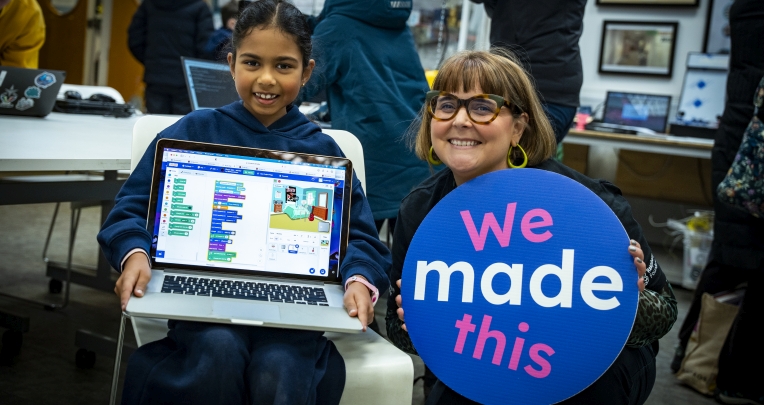 A school girl standing and holding a laptop next to a teacher