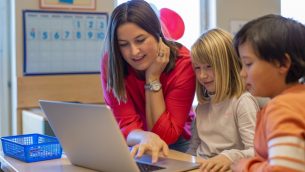 A teacher looking at a laptop with two primary school children