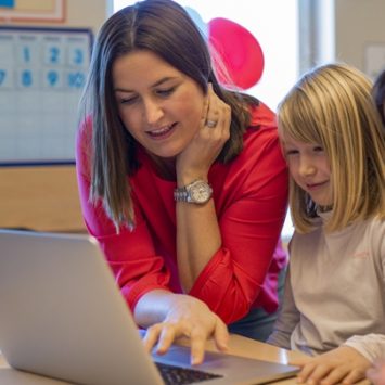 A teacher looking at a laptop with two primary school children