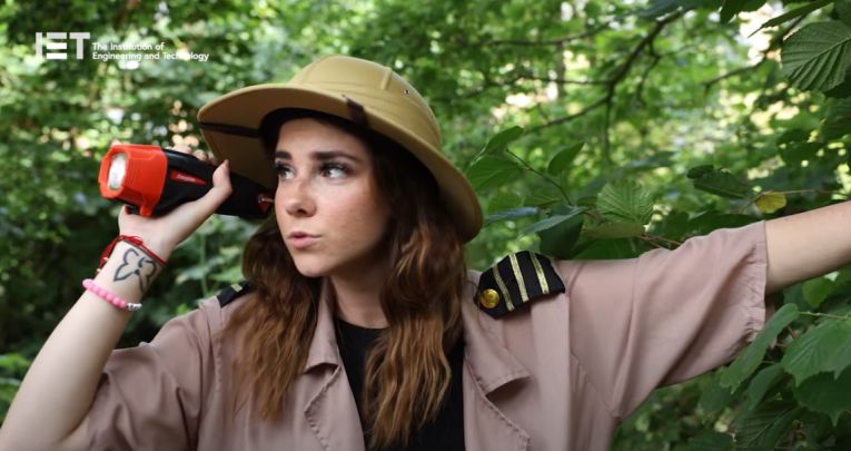 A woman dressed as an explorer holding a torch in a forest