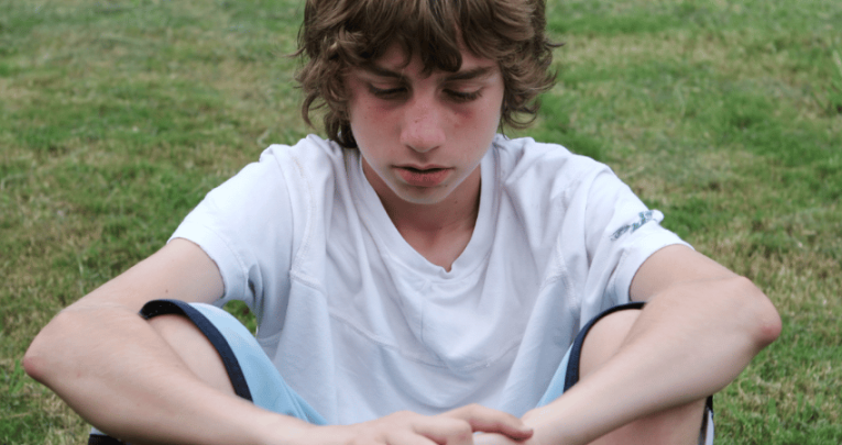White working class boy sitting on field