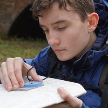 A student with a rucksack using a compass