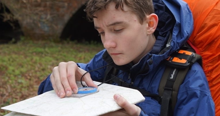 A student with a rucksack using a compass