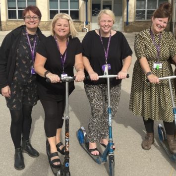 A group of teachers on scooters in a school playground