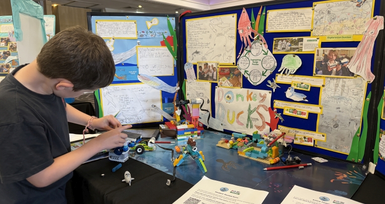 A young boy building LEGO in front of a poster display