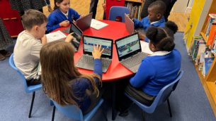 Primary school pupils sitting at a desk using Sumdog on laptops