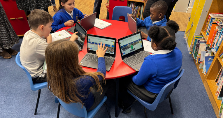 Primary school pupils sitting at a desk using Sumdog on laptops